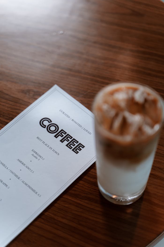Iced coffee placed on a wooden table beside a menu, offering a cozy cafe vibe.