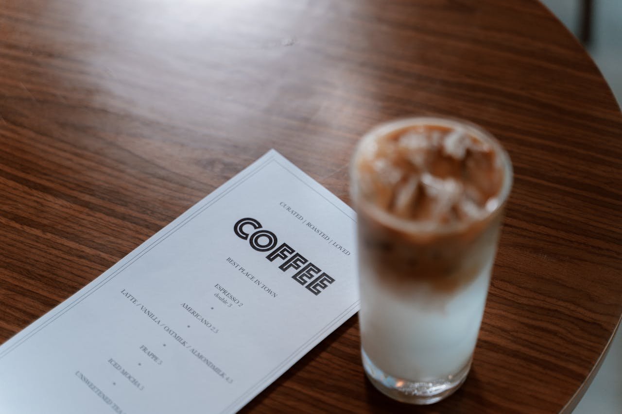 A refreshing iced coffee next to a menu on a wooden table, perfect for cafe vibes.