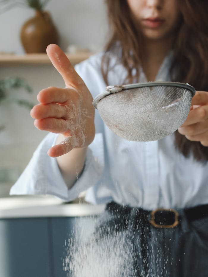 Close-up of a woman sifting flour in a bright kitchen, capturing a moment of domestic baking.