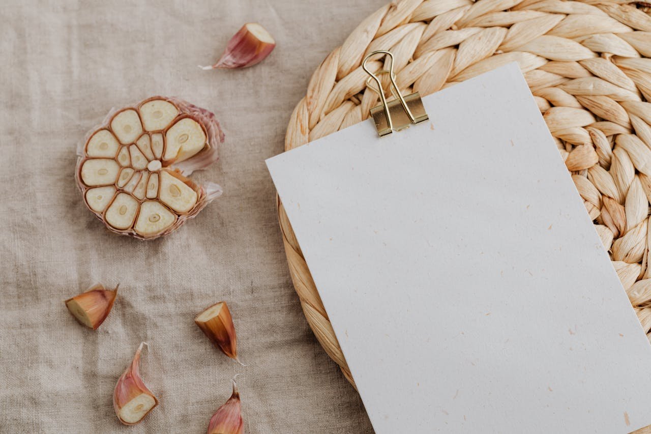 A rustic culinary scene featuring garlic cloves and a blank menu on a woven mat, perfect for recipe concepts.